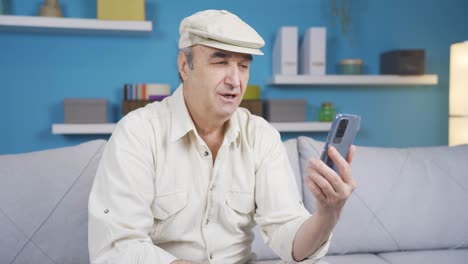 Abuelo-Anciano-Sentado-En-Un-Sofá-Disfrutando-En-Línea-En-La-Aplicación-Web-Del-Teléfono-Móvil.